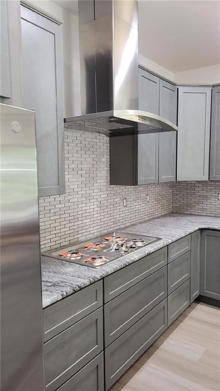 104 Lakeshore Dr, Kimberling City, MO 65686 - kitchen with wall chimney range hood, appliances with stainless steel finishes, gray cabinetry, backsplash, and light stone countertops
