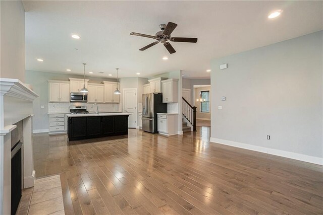 14446 Houston St, Olathe, KS 66061 - unfurnished living room with a fireplace with flush hearth, a ceiling fan, wood finished floors, stairs, and recessed lighting