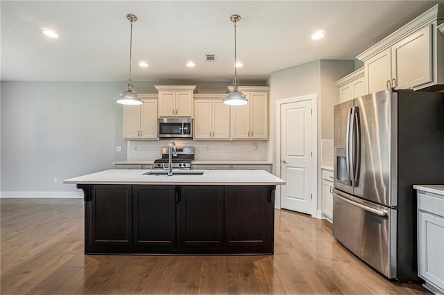 14446 Houston St, Olathe, KS 66061 - kitchen with stainless steel appliances, light countertops, wood finished floors, backsplash, and a kitchen island with sink
