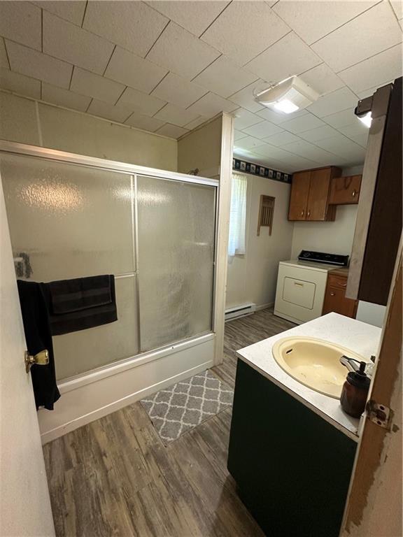 317 Chrissenger St, Burlington Junction, MO 64428 - full bath with washer / dryer, wood finished floors, vanity, bath / shower combo with glass door, and a baseboard heating unit
