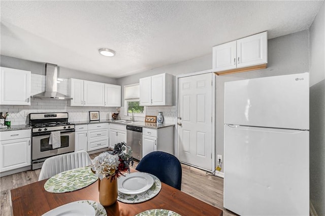 5117 Palmer Dr, Kansas City, MO 64129 - kitchen with stainless steel appliances, wall chimney exhaust hood, light wood-style floors, white cabinets, and a textured ceiling