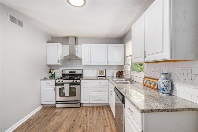 5117 Palmer Dr, Kansas City, MO 64129 - kitchen featuring wall chimney range hood, appliances with stainless steel finishes, light wood finished floors, and white cabinets