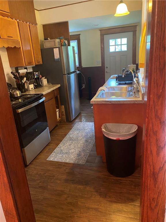 4020 Campbell St, Kansas City, MO 64110 - kitchen featuring appliances with stainless steel finishes, dark wood-style flooring, brown cabinetry, light countertops, and a peninsula