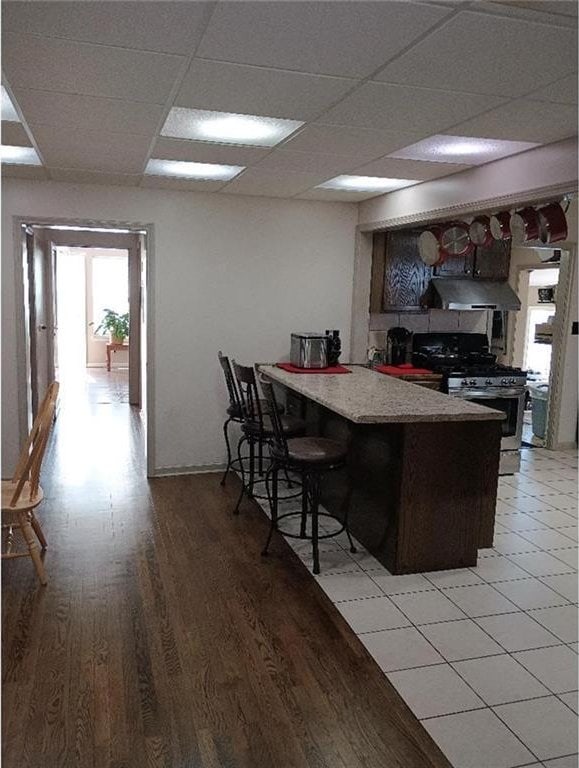 1712 S Hands St, Independence, MO 64055 - kitchen featuring stainless steel range with gas cooktop, extractor fan, light wood finished floors, a peninsula, and a paneled ceiling