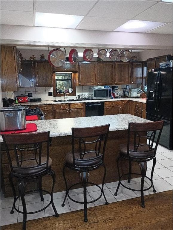 1712 S Hands St, Independence, MO 64055 - kitchen featuring black appliances, a paneled ceiling, a kitchen bar, a peninsula, and light tile patterned floors
