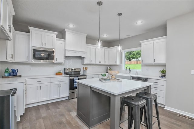 6118 Lewis Dr, Shawnee, KS 66226 - kitchen featuring appliances with stainless steel finishes, a breakfast bar area, wood finished floors, white cabinetry, and a kitchen island