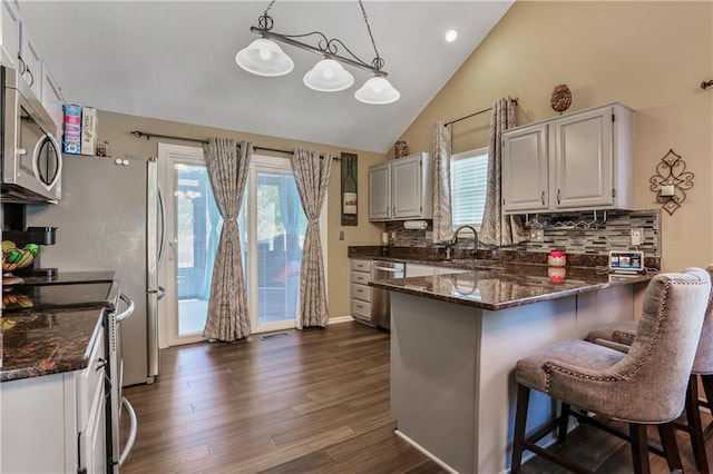 1641 N Hunter Dr, Olathe, KS 66061 - kitchen featuring appliances with stainless steel finishes, a peninsula, dark stone counters, backsplash, and dark wood-style flooring