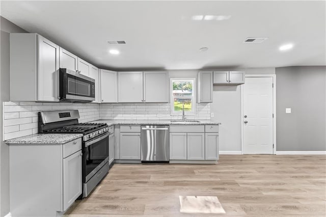 5513 Hardy Ave, Raytown, MO 64133 - kitchen featuring appliances with stainless steel finishes, decorative backsplash, light stone counters, light wood finished floors, and recessed lighting