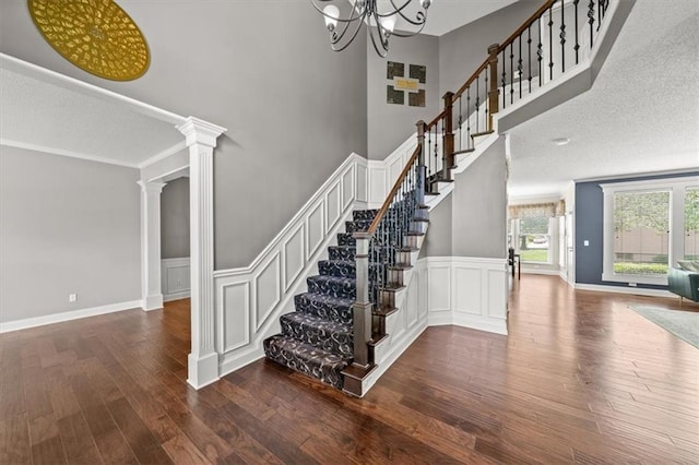 11927 W 131st Ter, Overland Park, KS 66213 - staircase featuring wood finished floors, wainscoting, ornate columns, a chandelier, and a decorative wall
