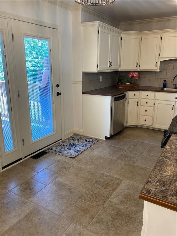 7909 Appleton Ave, Raytown, MO 64138 - kitchen featuring dishwasher, dark countertops, white cabinets, ornamental molding, and backsplash