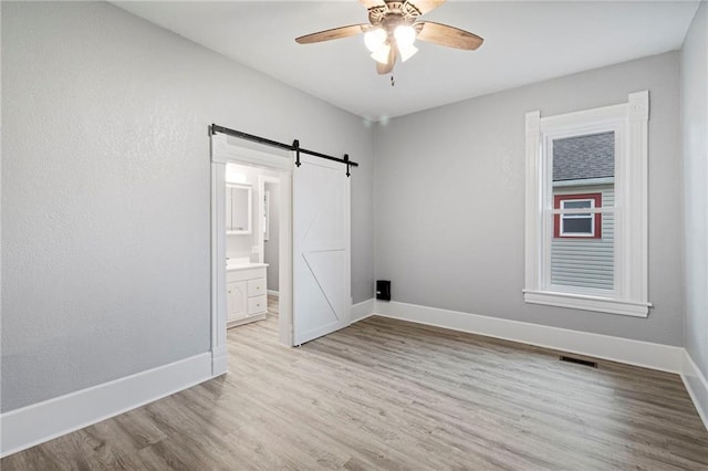 306 W 4th St, Cameron, MO 64429 - unfurnished bedroom with light wood-type flooring, a barn door, ensuite bath, and ceiling fan