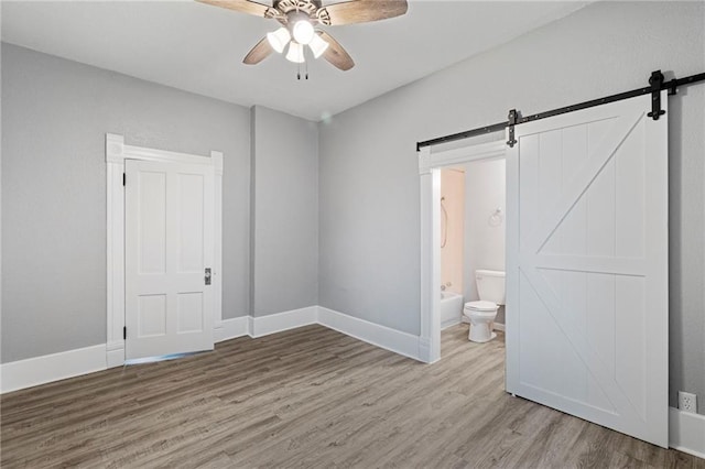 306 W 4th St, Cameron, MO 64429 - unfurnished bedroom with a barn door, wood finished floors, connected bathroom, and a ceiling fan