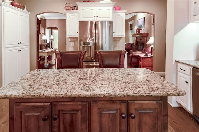 1310 Norfolk Dr, Harrisonville, MO 64701 - kitchen featuring arched walkways, stainless steel fridge with ice dispenser, a kitchen island, white cabinets, and light stone countertops