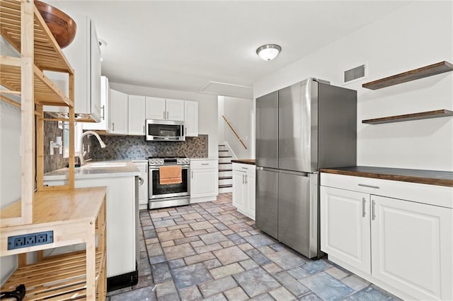 331 E 100th Ter, Kansas City, MO 64114 - kitchen with appliances with stainless steel finishes, open shelves, white cabinetry, decorative backsplash, and light stone finish floors