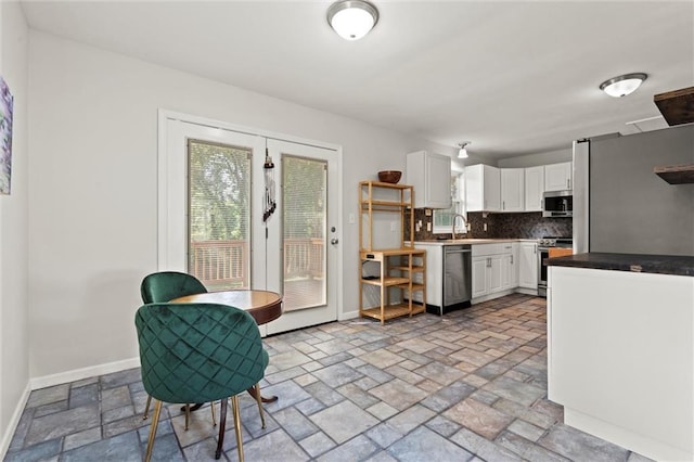 331 E 100th Ter, Kansas City, MO 64114 - kitchen featuring appliances with stainless steel finishes, white cabinets, stone tile flooring, backsplash, and healthy amount of natural light