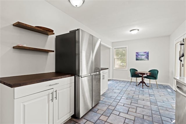 331 E 100th Ter, Kansas City, MO 64114 - kitchen with appliances with stainless steel finishes, light stone finish floors, white cabinets, open shelves, and butcher block countertops