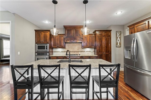 4890 NW Linder Ln, Riverside, MO 64150 - kitchen featuring appliances with stainless steel finishes, backsplash, dark wood finished floors, an island with sink, and a kitchen breakfast bar