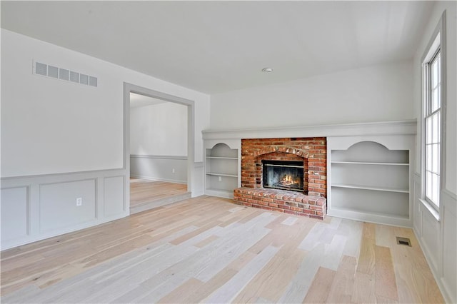 16117 W 125th Ter, Olathe, KS 66062 - unfurnished living room featuring healthy amount of natural light, light wood-style floors, built in shelves, a decorative wall, and a wainscoted wall