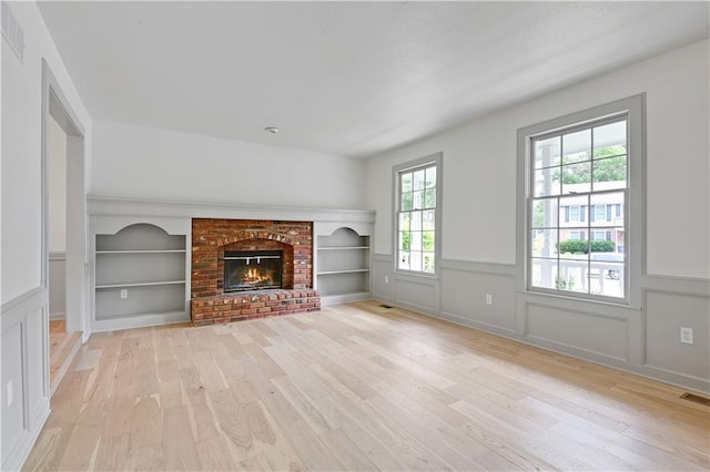 16117 W 125th Ter, Olathe, KS 66062 - unfurnished living room featuring light wood finished floors, a wainscoted wall, a fireplace, and built in shelves