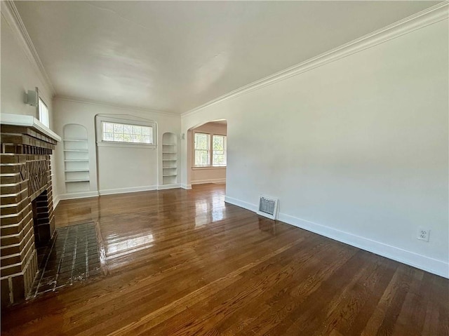 2416 E 70th St, Kansas City, MO 64132 - unfurnished living room with arched walkways, crown molding, a brick fireplace, built in shelves, and wood finished floors