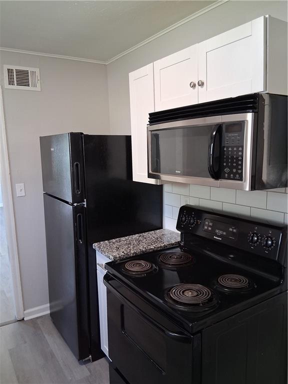 3304 Norton St, Kansas City, MO 64128 - kitchen with black electric range oven, stainless steel microwave, wood finished floors, backsplash, and white cabinets