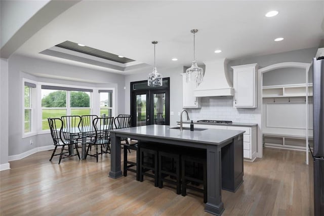 14423 N 145th St, Basehor, KS 66007 - kitchen featuring custom range hood, white cabinetry, backsplash, a center island with sink, and wood finished floors