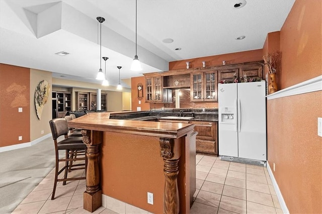 14409 Grandview St, Overland Park, KS 66221 - kitchen featuring white refrigerator with ice dispenser, brown cabinetry, a breakfast bar, light tile patterned flooring, and glass insert cabinets