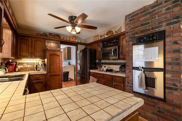 25421 Marel Rd, Excelsior Springs, MO 64024 - kitchen featuring black appliances, tile countertops, a ceiling fan, a peninsula, and a textured ceiling