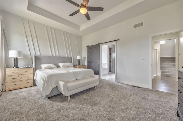 24976 W 87th St, Lenexa, KS 66227 - bedroom with a barn door, light colored carpet, a tray ceiling, connected bathroom, and a ceiling fan