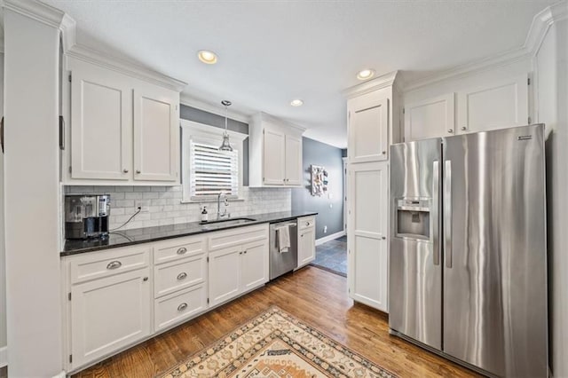 1295 W 71st Ter, Kansas City, MO 64114 - kitchen featuring appliances with stainless steel finishes, white cabinetry, wood finished floors, backsplash, and decorative light fixtures