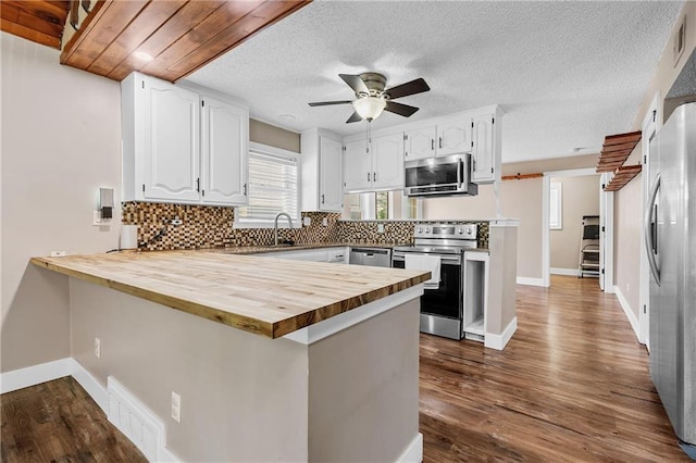 6727 Harvard Ave, Raytown, MO 64133 - kitchen featuring stainless steel appliances, wood counters, a peninsula, white cabinetry, and backsplash