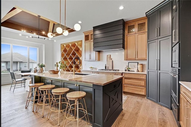 18501 Mohawk Ln, Overland Park, KS 66085 - kitchen featuring premium range hood, light wood finished floors, stainless steel appliances, wooden counters, and an island with sink