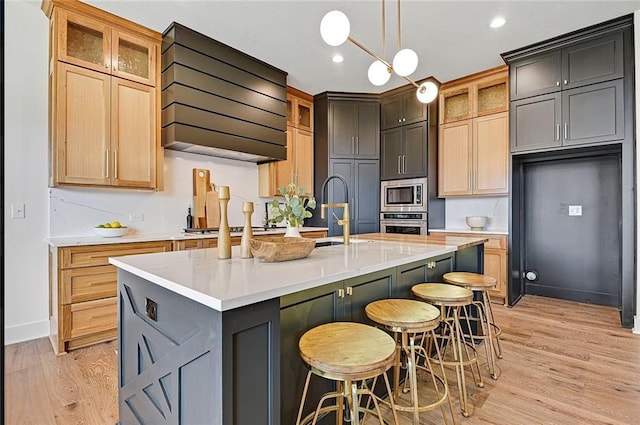 18501 Mohawk Ln, Overland Park, KS 66085 - kitchen with custom exhaust hood, stainless steel appliances, light wood-style floors, a kitchen island with sink, and light countertops