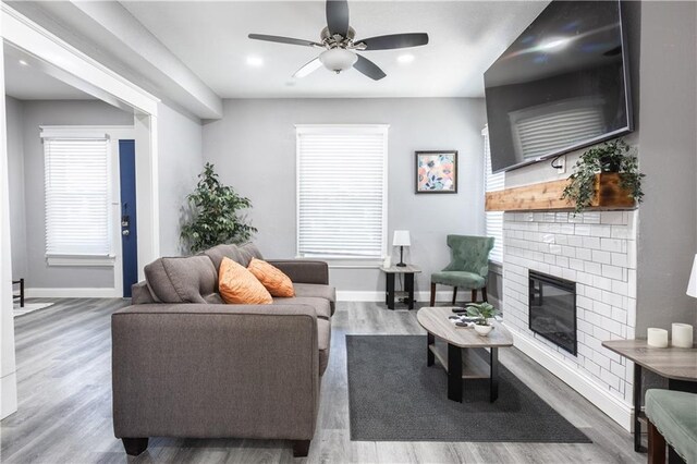 3221 E 11th St, Kansas City, MO 64127 - living area featuring a brick fireplace, ceiling fan, wood finished floors, and plenty of natural light