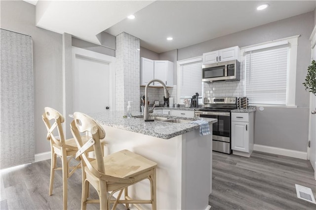 3221 E 11th St, Kansas City, MO 64127 - kitchen with stainless steel appliances, a breakfast bar area, decorative backsplash, light stone countertops, and wood finished floors