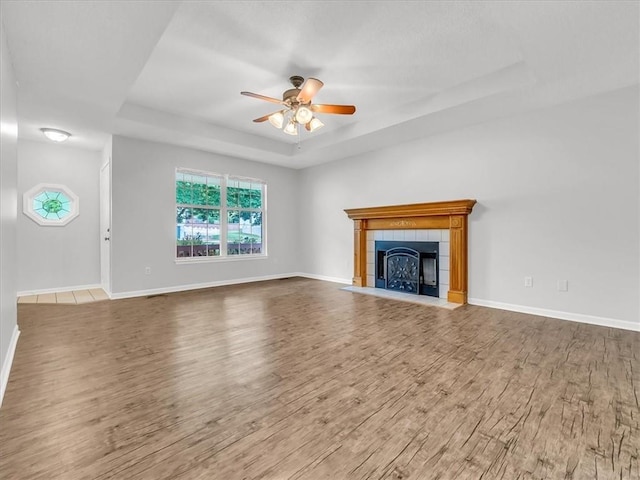 1914 S Leslie Dr, Independence, MO 64055 - unfurnished living room featuring a raised ceiling, a ceiling fan, wood finished floors, and a tile fireplace