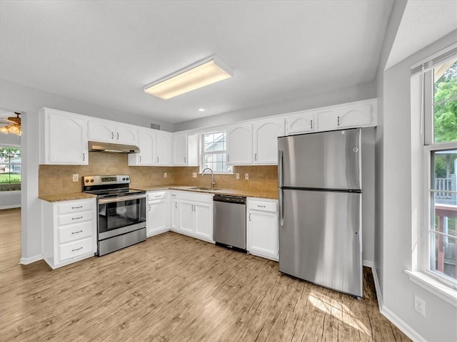 1914 S Leslie Dr, Independence, MO 64055 - kitchen featuring stainless steel appliances, under cabinet range hood, white cabinets, decorative backsplash, and light wood-style flooring