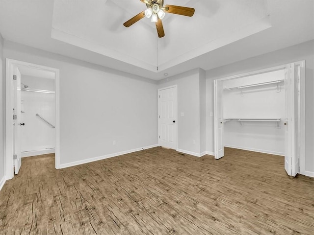 1914 S Leslie Dr, Independence, MO 64055 - unfurnished bedroom with a tray ceiling, wood finished floors, and ceiling fan