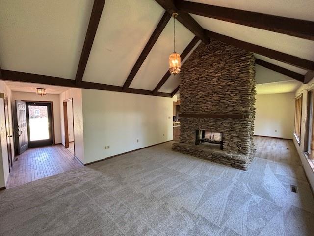 603 Lakeside Ct, Girard, KS 66743 - unfurnished living room with carpet flooring, beam ceiling, a stone fireplace, high vaulted ceiling, and a chandelier