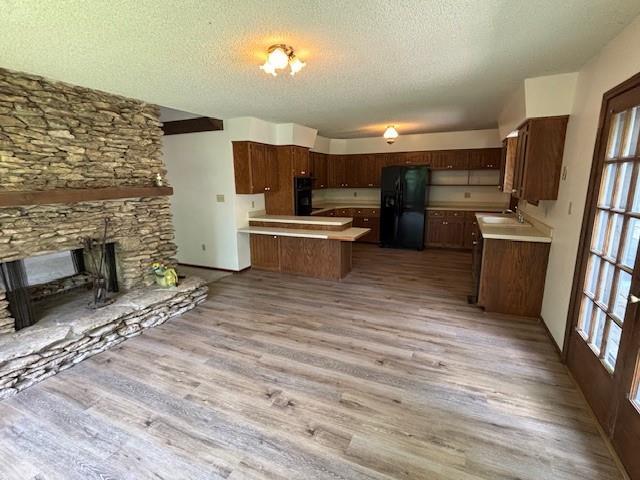 603 Lakeside Ct, Girard, KS 66743 - kitchen with black appliances, light wood-style floors, a textured ceiling, light countertops, and a fireplace