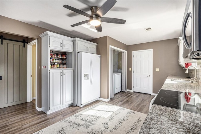 1433 Haskell Rd, Williamsburg, KS 66095 - kitchen with white fridge with ice dispenser, stainless steel microwave, a barn door, wood finished floors, and a ceiling fan