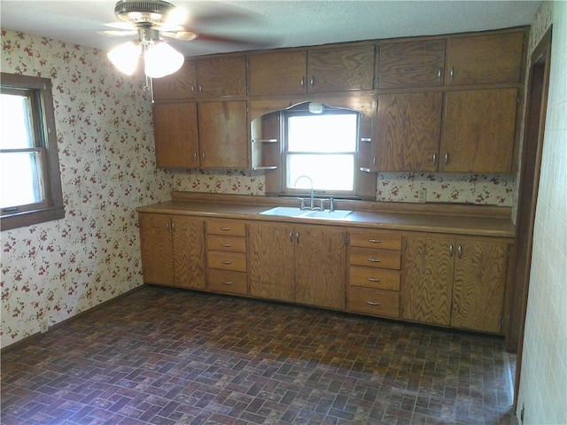 1022 Sycamore St, Humboldt, KS 66748 - kitchen featuring brick patterned flooring, wallpapered walls, a ceiling fan, and brown cabinetry