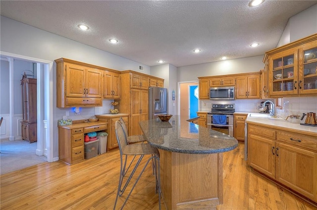 11580 S Skyview Ln, Olathe, KS 66061 - kitchen featuring appliances with stainless steel finishes, a textured ceiling, a kitchen island, a kitchen bar, and brown cabinets