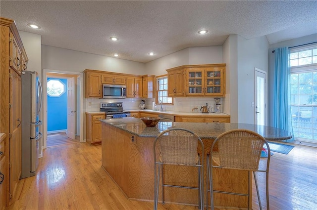 11580 S Skyview Ln, Olathe, KS 66061 - kitchen featuring stainless steel appliances, a textured ceiling, backsplash, light wood-style floors, and glass insert cabinets