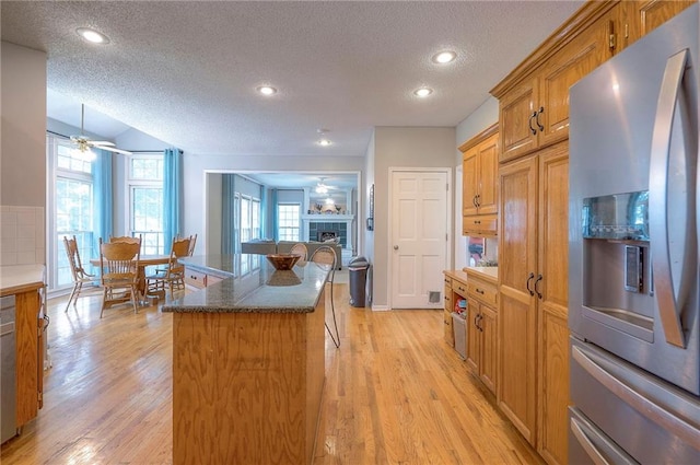 11580 S Skyview Ln, Olathe, KS 66061 - kitchen featuring stainless steel fridge, a textured ceiling, a tile fireplace, light wood-type flooring, and a kitchen island