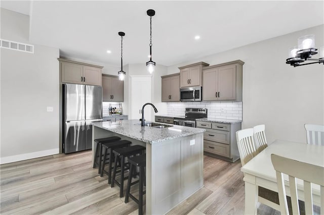 307 S Wilson St, Archie, MO 64725 - kitchen with stainless steel appliances, light wood-type flooring, gray cabinetry, decorative backsplash, and a breakfast bar area