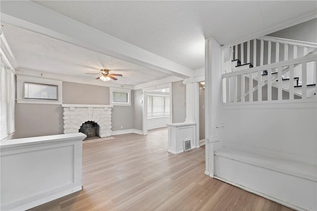 3544 College Ave, Kansas City, MO 64128 - unfurnished living room featuring ceiling fan, a textured ceiling, light wood-style flooring, a stone fireplace, and ornamental molding