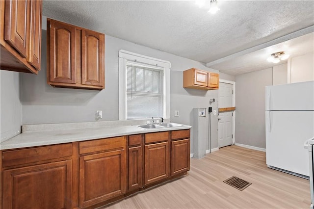 3544 College Ave, Kansas City, MO 64128 - kitchen featuring freestanding refrigerator, a textured ceiling, light countertops, light wood-style flooring, and brown cabinetry