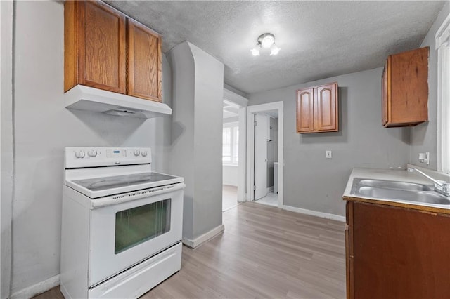 3544 College Ave, Kansas City, MO 64128 - kitchen with electric range, under cabinet range hood, brown cabinets, light wood-type flooring, and a textured ceiling