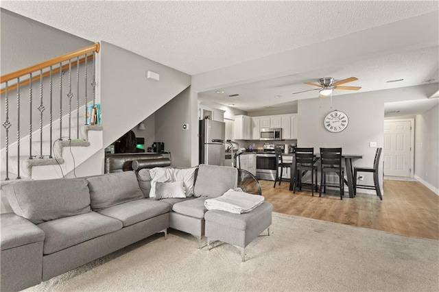 820 Peach Tree Ln, Blue Springs, MO 64064 - living area featuring stairway, a ceiling fan, light colored carpet, light wood-style floors, and a textured ceiling